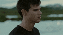 a young man in a black shirt stands in front of a lake