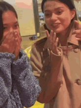two girls are sitting next to each other and one is covering her mouth with her hand