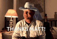 a man in a cowboy hat is sitting in front of a lamp and says thanks matt
