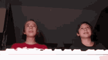 two young boys are sitting at a keyboard in a dark room looking up .