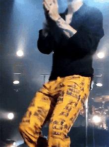 a man wearing a black shirt and yellow pants stands on a stage