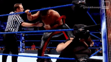 a referee is standing in a wrestling ring watching a wrestler fight another wrestler .