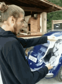 a man in a black sweatshirt is putting a picture of a woman on a car