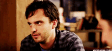 a man in a plaid shirt is sitting at a table and looking at another man .