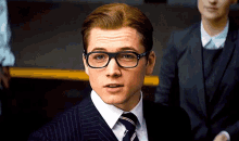 a man in a suit and tie wearing glasses looks at the camera