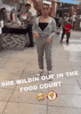 a woman is standing on a sidewalk in a food court in a shopping mall .