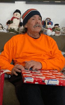 a man in an orange sweater is sitting on a couch with a christmas present