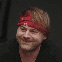 a man wearing a red bandana with the letter g on it smiles
