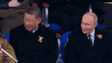 a man in a suit and tie sits next to another man in a suit and tie