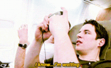 a man sitting on an airplane playing a video game and says i know i 'm waiting