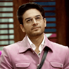 a man wearing glasses and a pink jacket is looking at something
