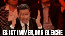 a man in a suit and tie is clapping his hands in the air .