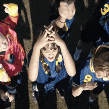 a girl in a blue jersey with the number 9 on it holds her hands to her head