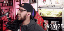 a man wearing glasses and a hat is sitting in front of a microphone with the number 592/625 on the bottom right