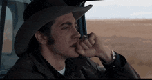a man wearing a cowboy hat is sitting in a car smoking a cigarette