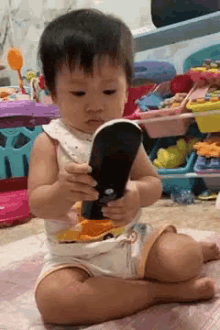 a baby is sitting on the floor holding a toy cell phone .