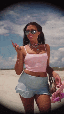 a woman in a pink tank top and blue shorts stands on a beach