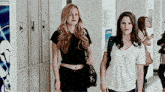 two girls are walking down a hallway with lockers