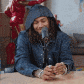 a man wearing a hooded jacket is sitting in front of a microphone and looking at his phone