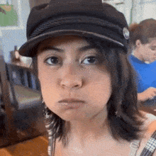 a woman wearing a black hat and earrings looks at the camera
