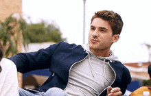 a young man wearing a blue jacket and a gray shirt is sitting on a couch .