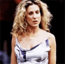 a woman with curly hair is wearing a white and blue dress and a necklace .