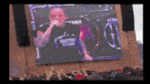 a man is singing into a microphone in front of a large screen that says tama on it .