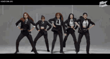 a group of women in tuxedos are dancing in front of a sign that says the k