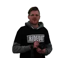 a man wearing a shirt that says " rideout " holds a camera