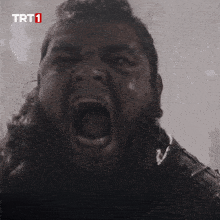 a man with a beard is screaming in front of a trt 1 logo