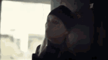 a woman in a black hat is leaning against a wall and talking on a cell phone .