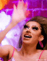 a drag queen is waving her hands in the air while wearing pink earrings