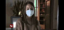 a woman wearing a face mask is sitting in front of a computer with tg2 written on the bottom of the screen