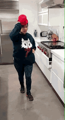 a woman wearing a sweater with a cat on it holds a red hat on her head