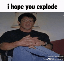a man sits on a couch with his hands folded and a caption that says i hope you explode