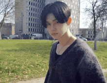 a young man wearing a black sweater stands in front of a large building