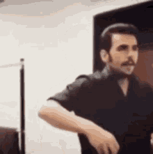 a man with a mustache is standing in a room with his hands in the air .