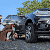 a man kneeling next to a black suv with the door open