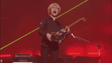 a man in a black shirt is playing a guitar in front of a green light