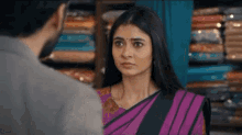 a woman in a purple saree is talking to a man in a store .