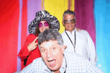 a man and two women pose for a photo in front of a colorful background