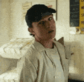a young man wearing a baseball cap and a white shirt is standing in a bedroom .