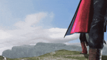 a person wearing a red cape stands in front of a mountain range