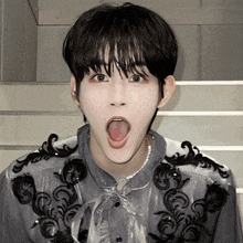 a young man with his tongue hanging out is wearing a gray shirt with black embroidery