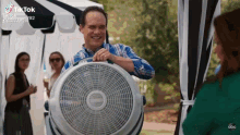a man is smiling while holding a fan in front of a tent