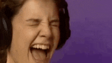 a woman wearing headphones is screaming with her mouth open and her eyes closed .