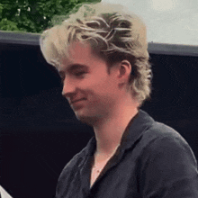 a young man with blonde hair is wearing a black shirt and earrings .