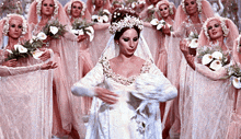 a woman in a wedding dress is surrounded by other women in pink dresses