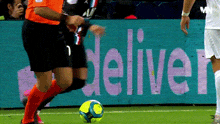 a soccer player is kicking a soccer ball in front of a sign that says deliver