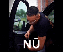 a man wearing glasses is getting out of a car with the word nu on the bottom right
